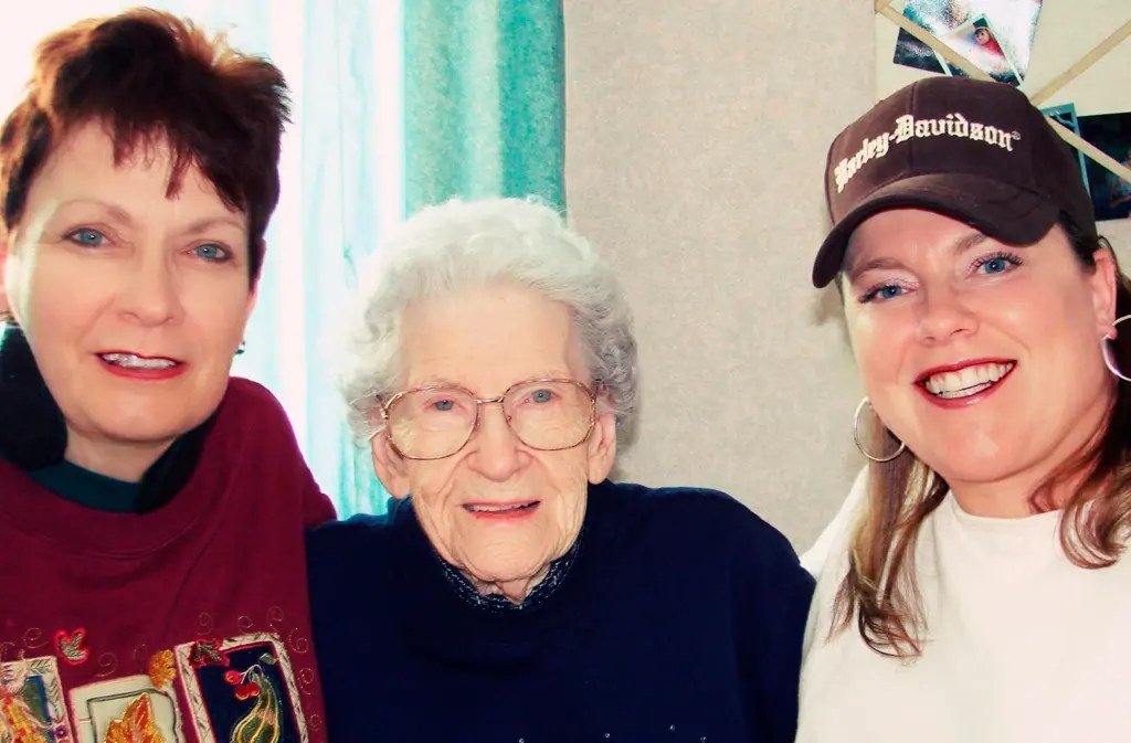 Three people pose and smile at the camera, with one wearing a cap reading "Harley-Davidson" and the person in the middle wearing glasses.