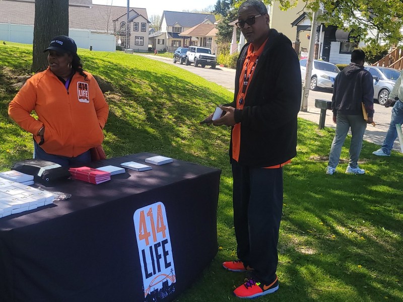 People stand on grass near a table with 414LIFE signs.