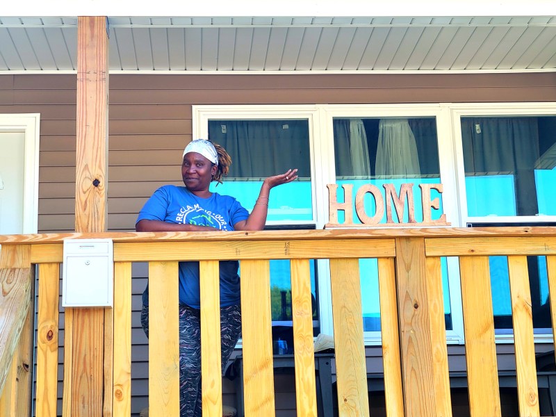Woman stands on porch of home.