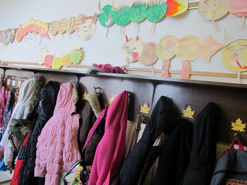 Children's coats hang on a rack under paper art of creatures on the wall.