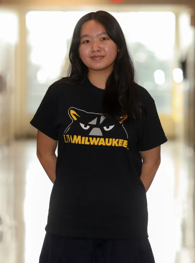 A person stands in a hallway wearing a shirt with a panther logo and the text "UWMILWAUKEE"