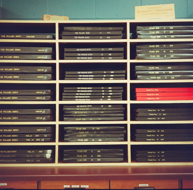 Shelves with items labeled "Pulaski News.” A plaque on top reads “In Memory of Bernard C. Olejniczak.”