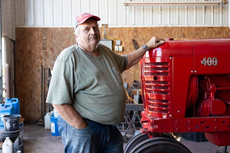 A person rests a hand on a red tractor marked "400" inside a building with buckets, containers and other items along the walls.