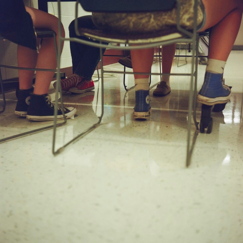 Feet of people wearing different shoes, including sneakers, are visible under classroom chairs.