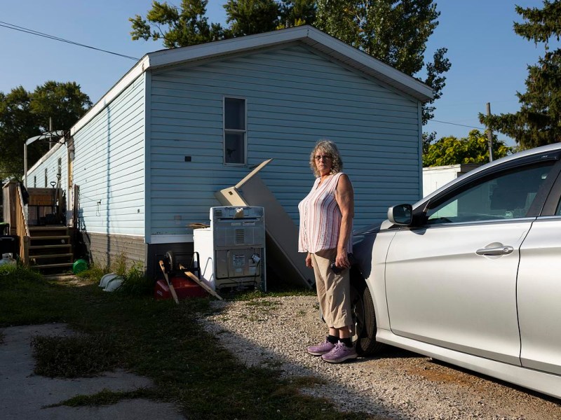 Person stands next to car and house.