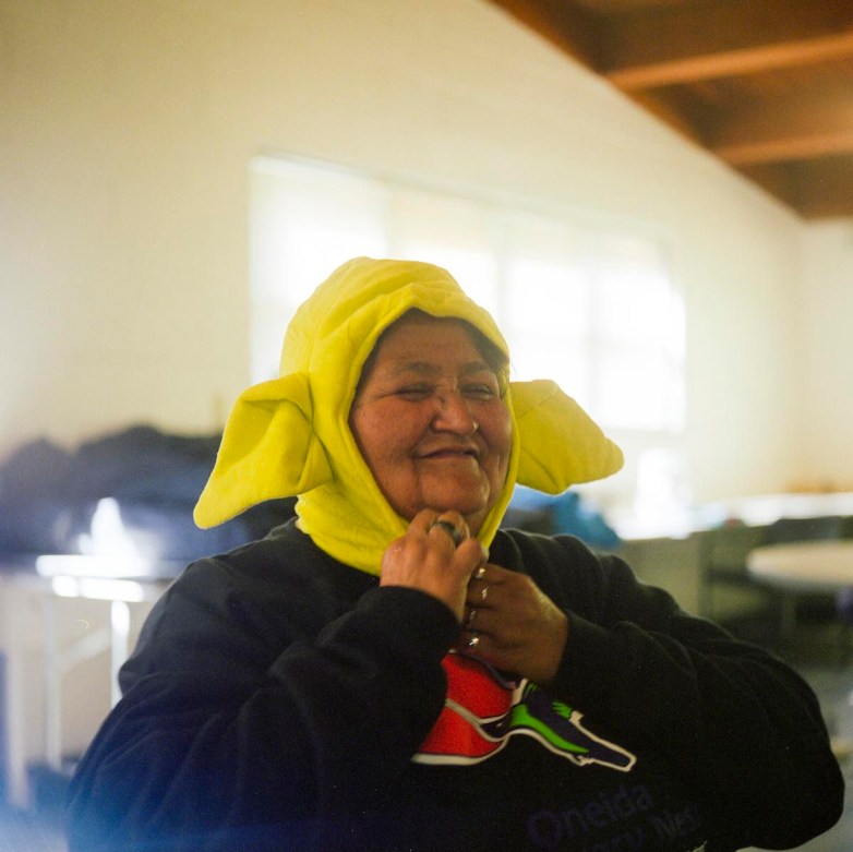 A person wearing a dark sweatshirt adjusts a light green hat with large fabric ears.