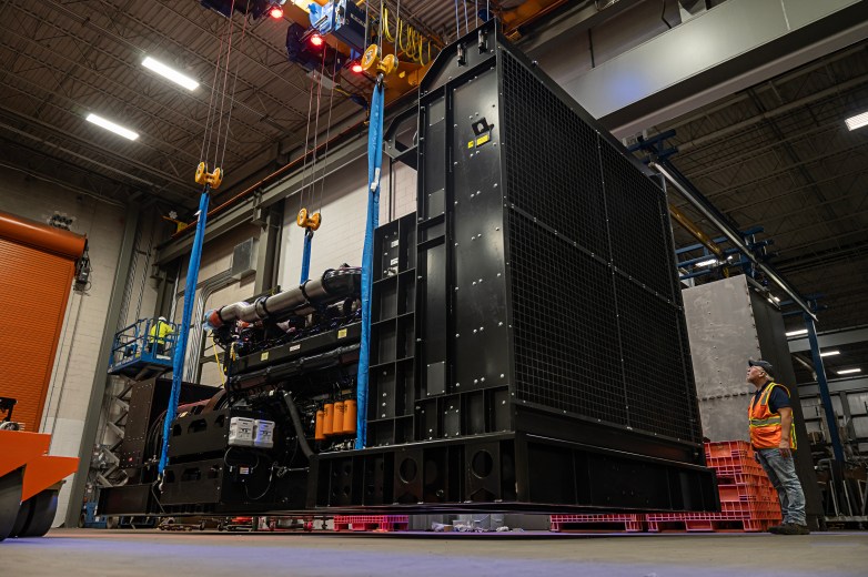 A person wearing a safety vest stands next to a large generator in a warehouse.