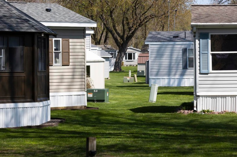 Rows of mobile homes with various colors line a grassy area with trees and utility boxes between them.