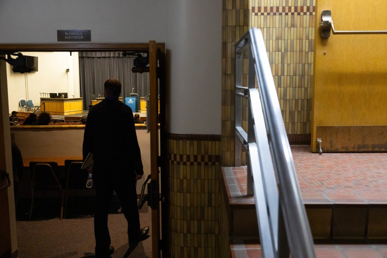 A person walks through a doorway labeled "McDANIELS AUDITORIUM" toward rows of seats and a stage with a podium and desks visible at the front