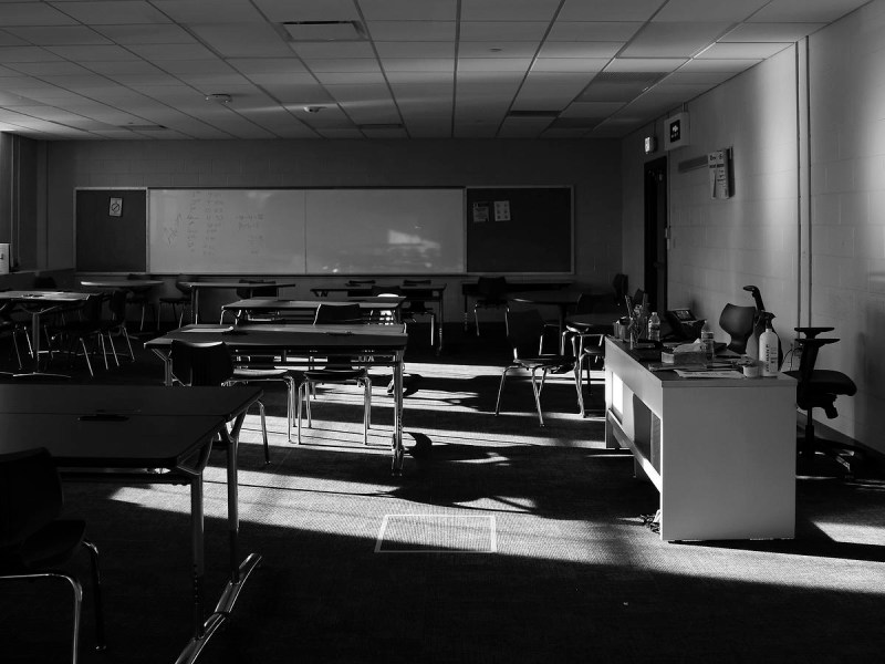 An empty classroom with rows of desks, a whiteboard and sunlight streaming onto the floor.