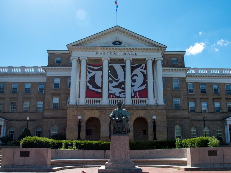 A statue of U.S. President Abraham Lincoln sits in front of Bascom Hall on the University of Wisconsin-Madison campus under a blue sky.