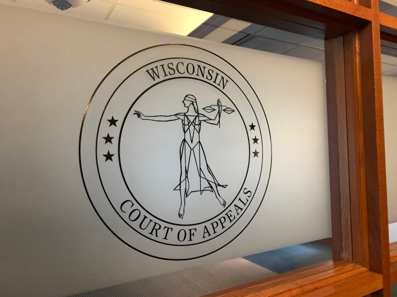 A frosted glass panel displays a circular image reading “WISCONSIN COURT OF APPEALS” with a blindfolded figure holding scales at the center and stars around the border.