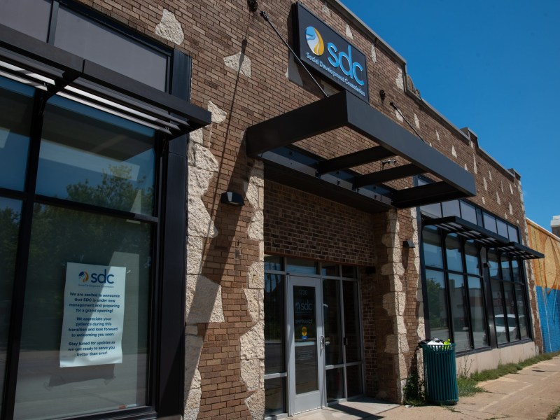 A brick building with a sign reading "sdc Social Development Commission" above the entrance and a poster in a window