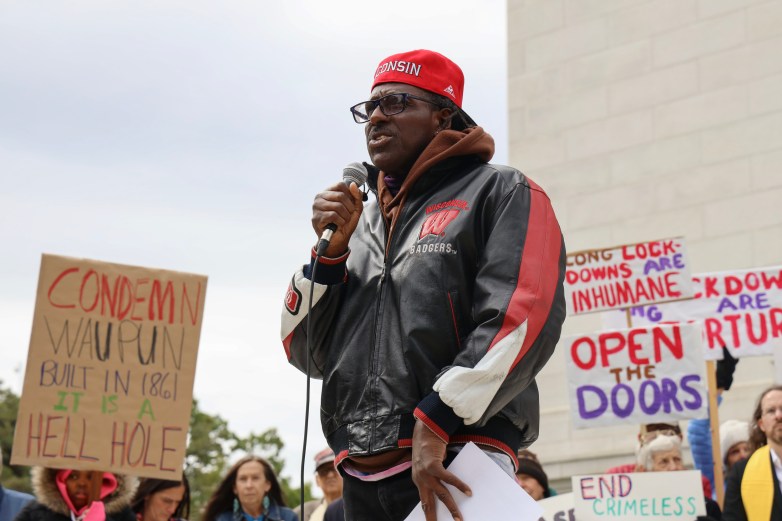 Former prisoner Talib Akbar speaks at a protest as others hold signs behind him.