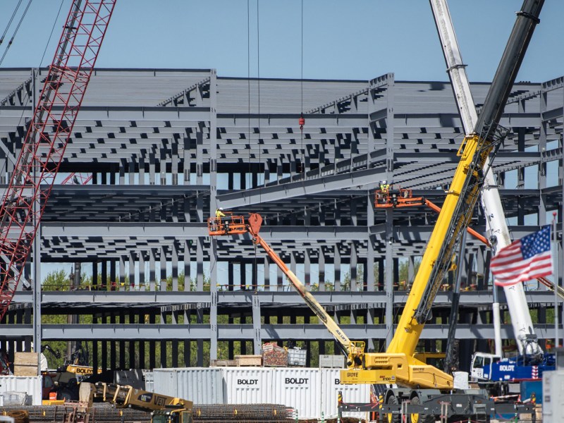 Big building under construction with cranes and an American flag in foreground