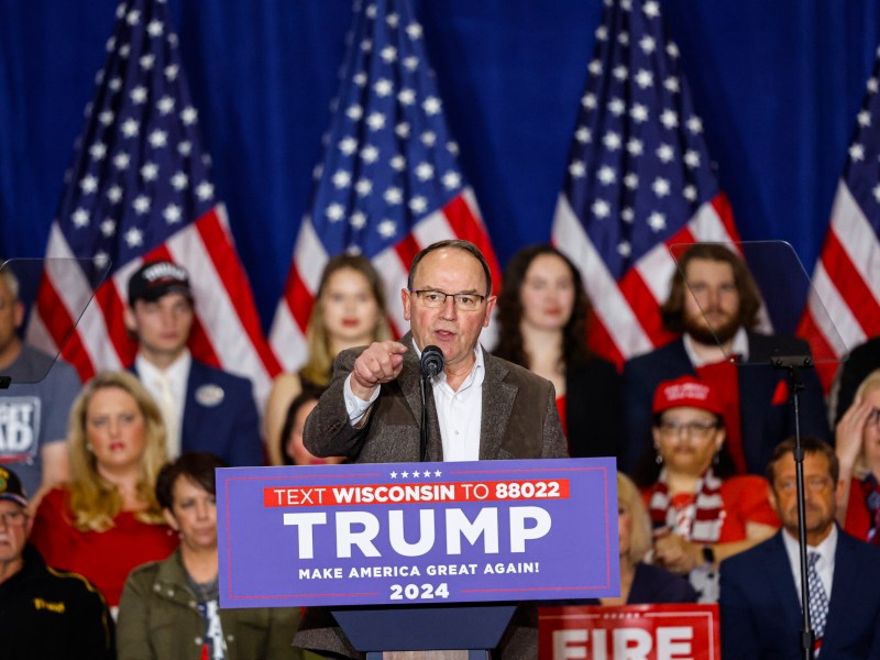 U.S. Rep. Tom Tiffany points and stands behind a podium that says “Trump make America great again”