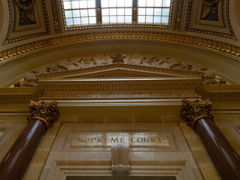 Ornate interior architecture with columns, gold detailing and a stone inscription reading "Supreme Court" under a skylight.